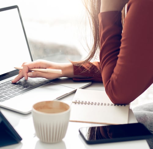 Woman searching for jobs on laptop with coffee and phone near her